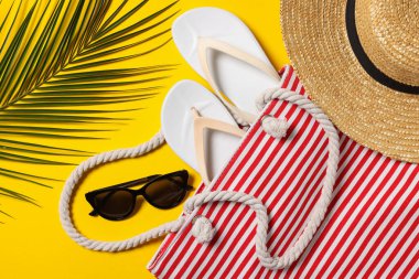 Sarı arka planda torba, palmiye yaprağı ve diğer plaj aksesuarlarıyla düz kompozisyon
