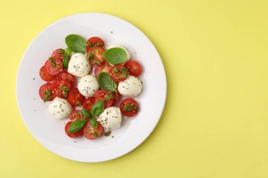 Domatesli Caprese salatası, mozzarella topları ve sarı arka planda fesleğen, üst manzara. Metin için boşluk