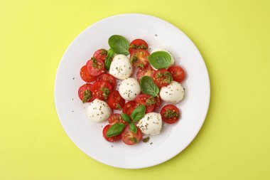 Domatesli Caprese salatası, mozzarella topları ve sarı arka planda fesleğen.
