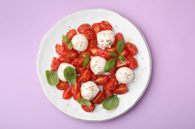 Domatesli Caprese salatası, mozzarella topları ve leylak arkaplanlı fesleğen.