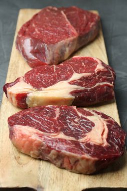 Gri masada çiğ et parçaları olan ahşap tahta, yakın plan.