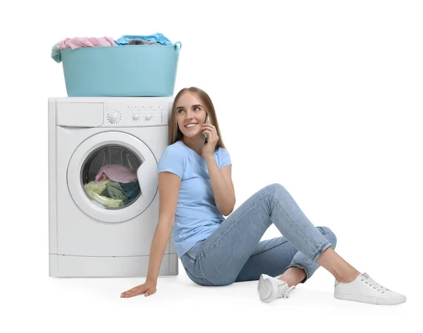 白い背景に対して洗濯機の近くのスマートフォンで話す美しい若い女性 — ストック写真