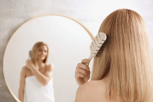 Woman brushing her hair near mirror in bathroom