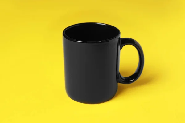 一个黄色背景的黑色陶瓷杯子 — 图库照片