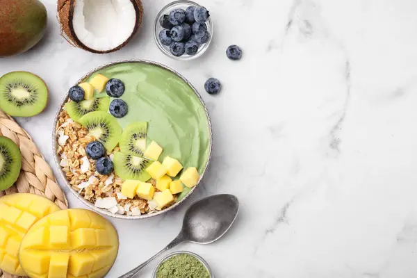 Tasty matcha smoothie bowl with fresh fruits and oatmeal served on white marble table, flat lay with space for text. Healthy breakfast