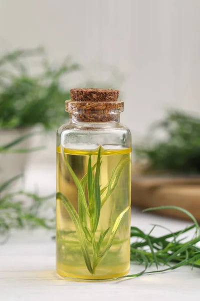 Bottle of essential oil and fresh tarragon leaves on white wooden table