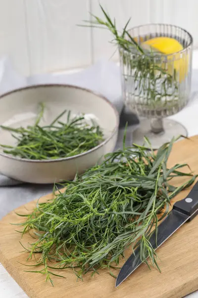 Fresh tarragon sprigs and knife on wooden board, closeup