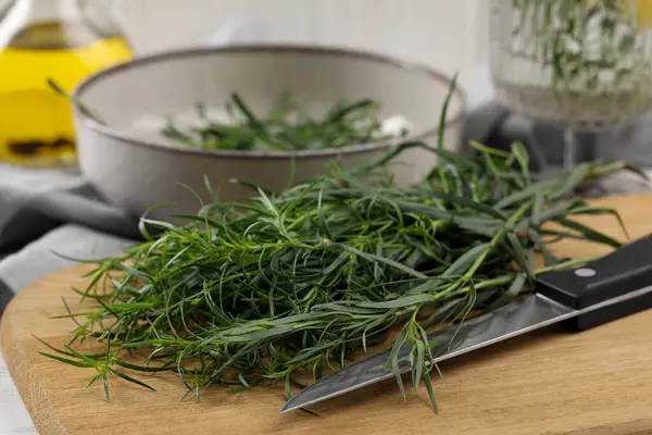 Fresh tarragon sprigs and knife on wooden board, closeup