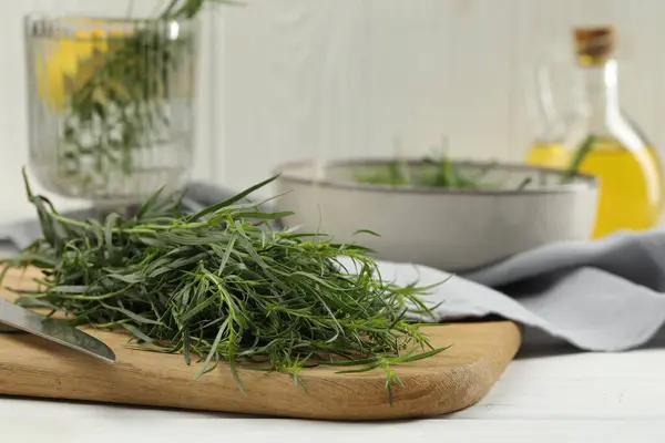Fresh tarragon sprigs and knife on white wooden table, closeup