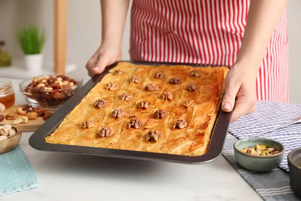 Woman holding baking pan of delicious baklava with walnuts above white table, closeup