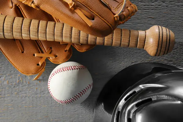 Baseball glove, bat, ball and batting helmet on grey wooden table, flat lay