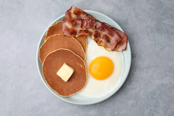 Tasty pancakes with fried egg and bacon on grey table, top view