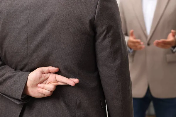 Employee crossing fingers behind his back while meeting with boss, closeup