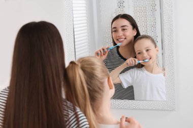 Anne ve kızı içeride aynanın yanında dişlerini fırçalıyorlar.
