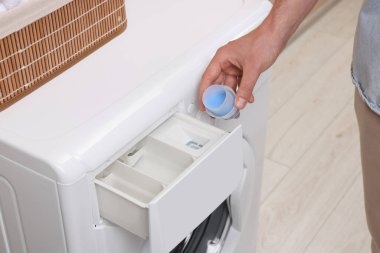 Kapaktan çamaşır makinesine kumaş yumuşatıcısı döken adam, yakın plan.