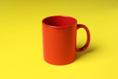 Sarı arkaplanda bir kırmızı seramik bardak.