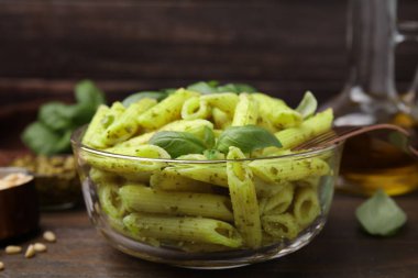 Pesto soslu lezzetli makarna ve ahşap masada fesleğen, yakın plan.