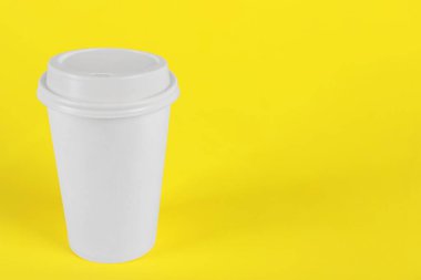 Sarı arka planda plastik kapaklı kağıt bardak, metin için boşluk. Kahve hazır.