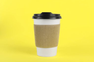 Sarı arka planda plastik kapaklı kağıt bardak. Kahve hazır.