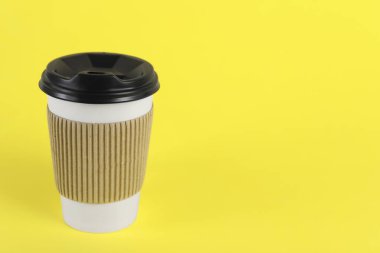 Sarı arka planda plastik kapaklı kağıt bardak, metin için boşluk. Kahve hazır.