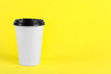 Sarı arka planda plastik kapaklı kağıt bardak, metin için boşluk. Kahve hazır.