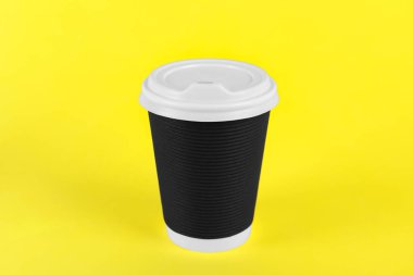 Sarı arka planda plastik kapaklı siyah kağıt bardak. Kahve hazır.