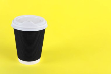Sarı arka planda plastik kapaklı siyah kağıt bardak, metin için boşluk. Kahve hazır.