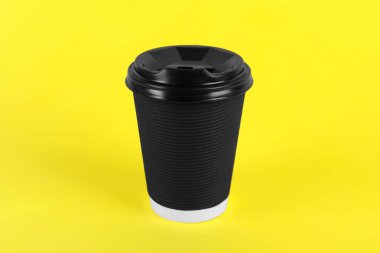 Sarı arka planda plastik kapaklı siyah kağıt bardak. Kahve hazır.