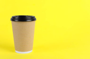 Sarı arka planda plastik kapaklı kağıt bardak, metin için boşluk. Kahve hazır.