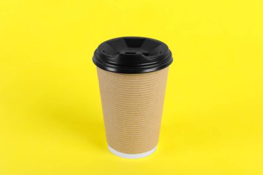 Sarı arka planda plastik kapaklı kağıt bardak. Kahve hazır.