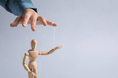 Woman pulling strings of puppet on light grey background, closeup. Space for text