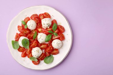 Domatesli Caprese salatası, mozzarella topları ve pembe arka planda fesleğen. Metin için boşluk