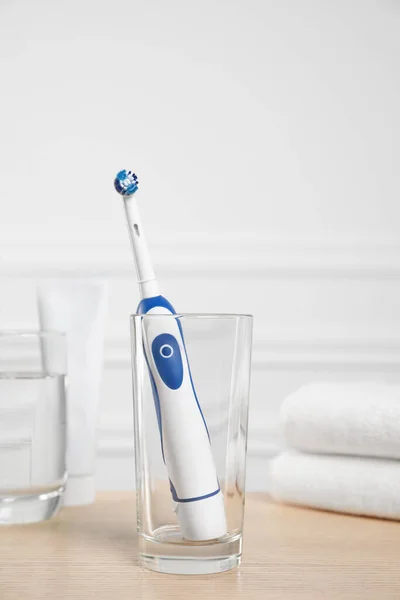 Electric toothbrush, glass of water and toiletries on wooden table