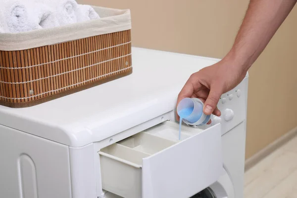 Man pouring fabric softener from cap into washing machine indoors, closeup