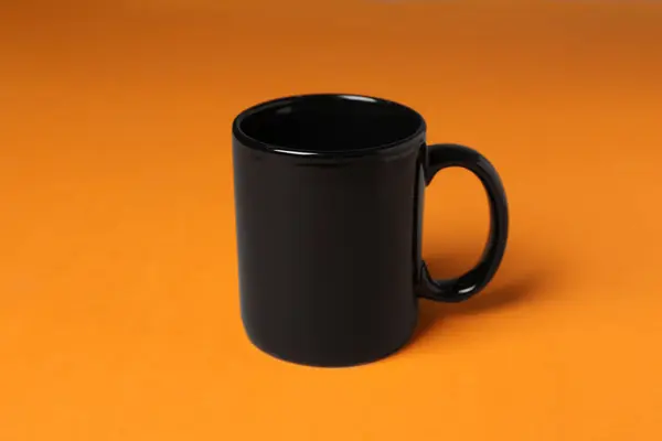 オレンジ色の背景に1つの黒いセラミックマグ — ストック写真