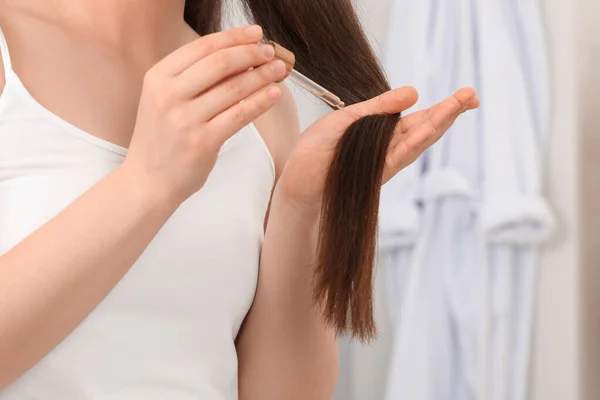 Woman applying essential oil onto hair on blurred background, closeup