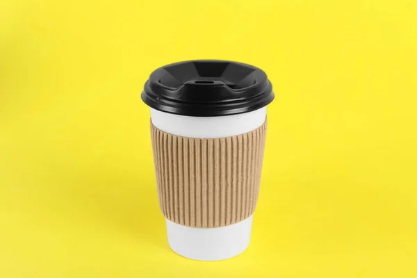 Paper cup with plastic lid on yellow background. Coffee to go