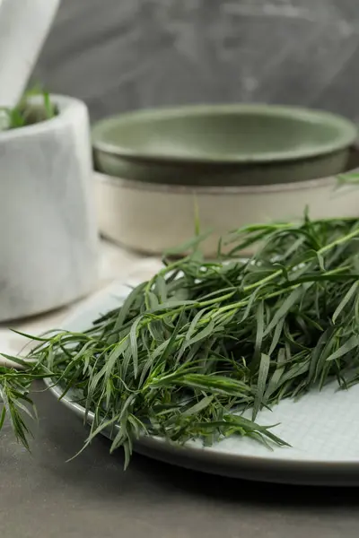 Plate with fresh tarragon leaves on grey table, closeup