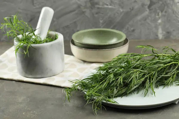 Plate and mortar with fresh tarragon leaves on grey table