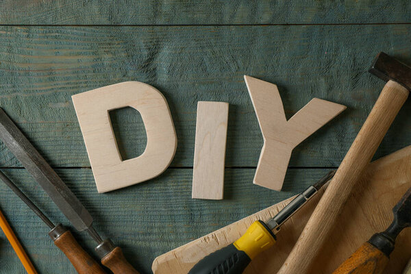 Abbreviation DIY made of letters and different tools on grey wooden table, flat lay