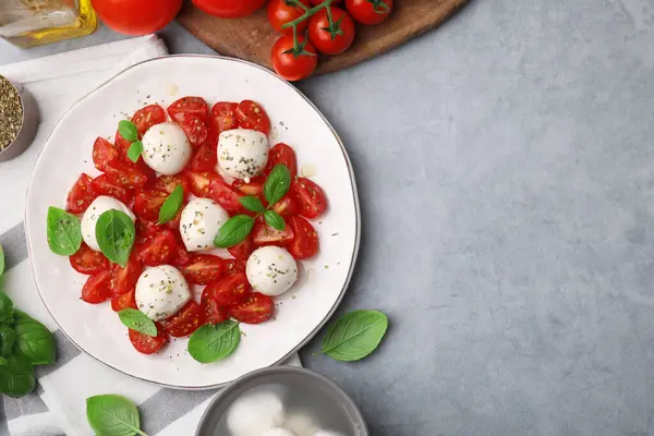 Domatesli Caprese salatası, mozzarella topları, fesleğen ve gri arka planda malzemeler, düz yatak. Metin için boşluk