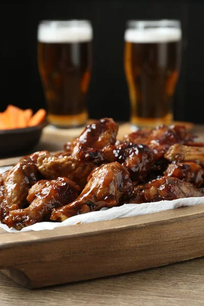 Tasty chicken wings served with beer on wooden table, closeup. Delicious snack