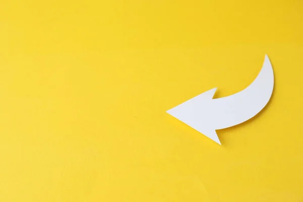 White curved paper arrow on yellow background, top view. Space for text