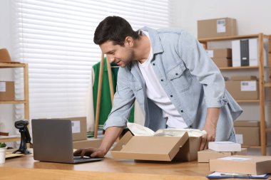 Ofiste çalışan paket ve dizüstü bilgisayarı olan bir satıcı. Çevrimiçi mağaza