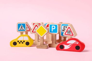 Ahşap yol işaretleri ve açık pembe arka planda arabalar. Çocuk oyuncağı.