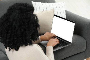 Evdeki kanepede dizüstü bilgisayar kullanan bir kadın.