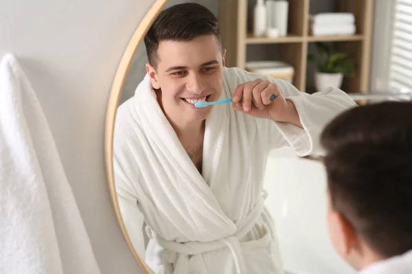 Man brushing his teeth with toothbrush near mirror in bathroom