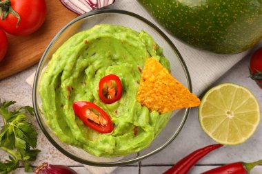 Bir kase lezzetli guacamole, cips ve malzemeler beyaz fayanslı masada, düz yerde.