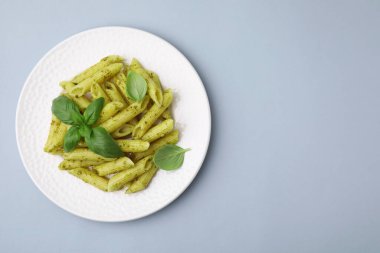 Pesto soslu lezzetli makarna ve açık gri arka planda fesleğen, üst manzara. Metin için boşluk