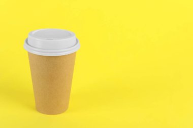 Sarı arka planda plastik kapaklı kağıt bardak, metin için boşluk. Kahve hazır.